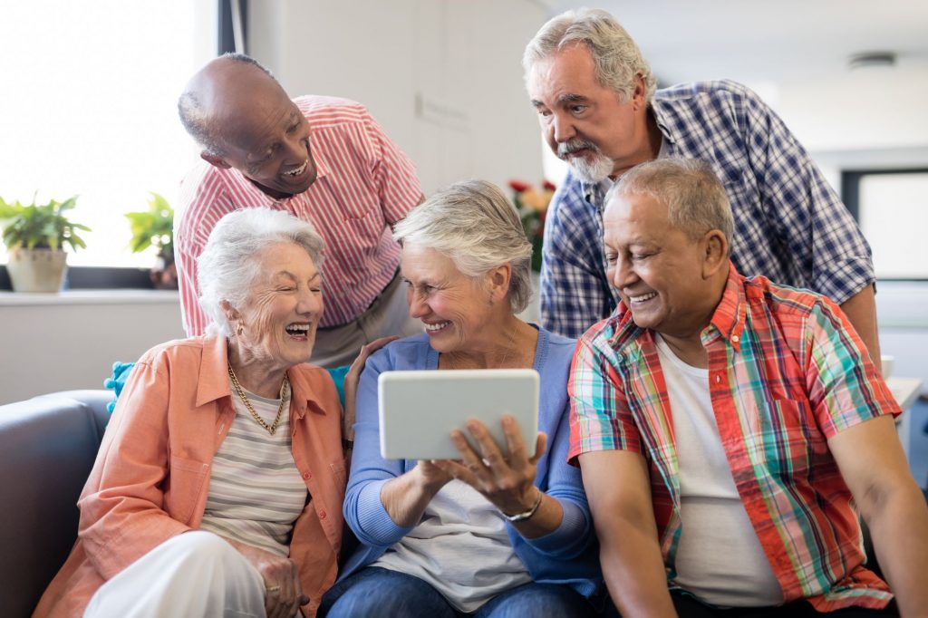 group of seniors sitting together and laughing using technology
