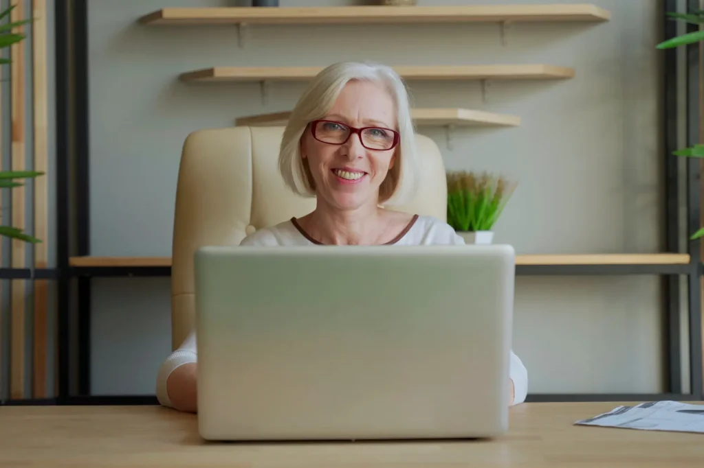 lady with glasses sitting at desk behind laptop, working senior