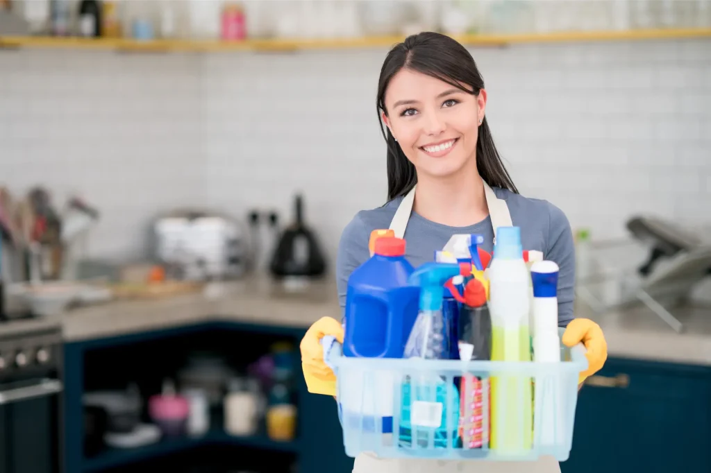 young asian female holding a basket of cleaning supplies and smiling, housekeeping