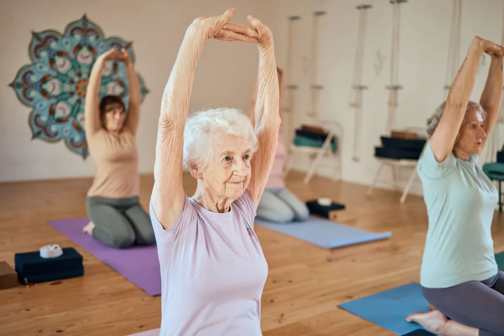 Elderly woman, yoga and stretching in class for healthy spiritual, mind and body wellness at the studio. Senior female in warm up arm stretch or pose in yoga class together for zen and health fitness