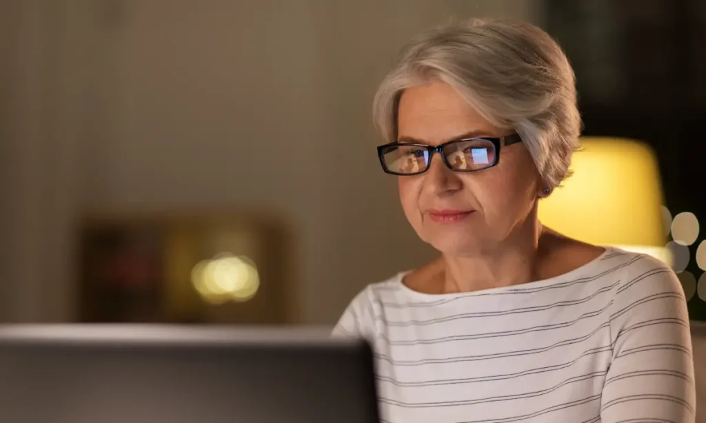 senior woman taking a class using a computer in the vening, monitor reflection in her glasses