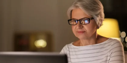 senior woman using a computer in the vening, monitor reflection in her glasses
