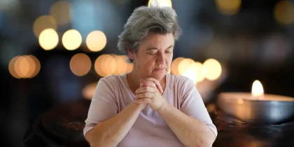 senior woman with eyes closed and praying near candles