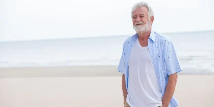 older senior man standing on the beach smiling, looking fulfilled, satisfied, content, happy