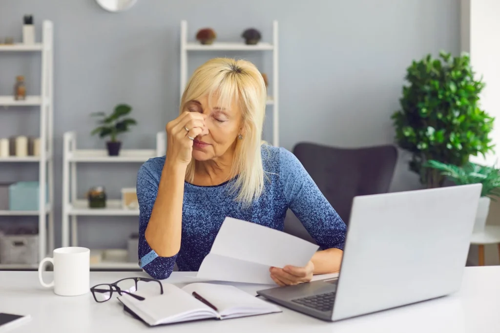 stressed senior woman looking at papers and computer squinting her eyes