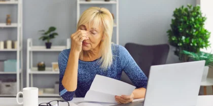 stressed senior woman looking at papers and computer squinting her eyes