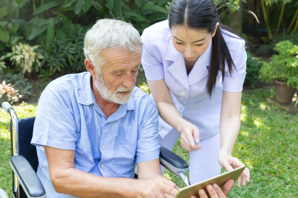 senior man in wheelchair outside looking at a care plan with an aide in an assisted living or nursing care facility