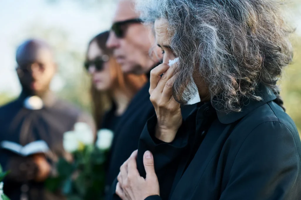 Senior woman with grey hair wiping tears with handkerchief at funeral of her relative or family member with a broken heart