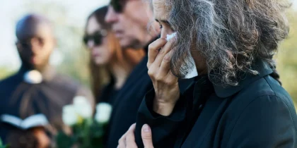 Senior woman with grey hair wiping tears with handkerchief at funeral of her relative or family member with a broken heart