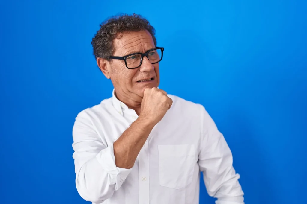 middle-aged retirement age hispanic man looking very worried on a solid blue background