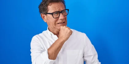 middle-aged retirement age hispanic man looking very worried on a solid blue background
